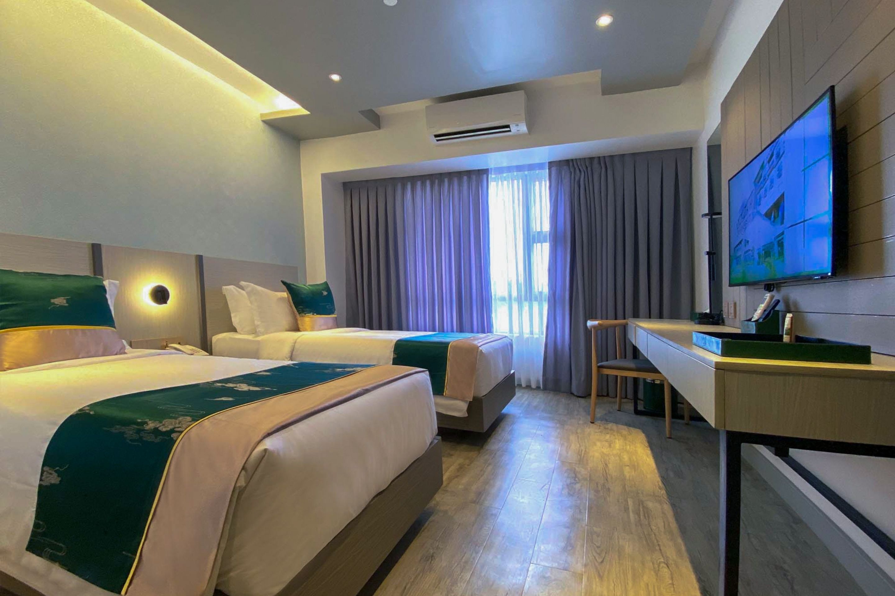 Une chambre d’hôtel avec deux lits, un bureau, une télévision et une grande fenêtre avec des rideaux.