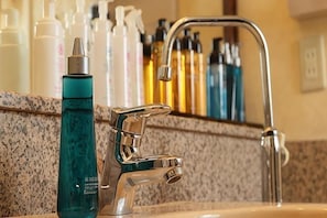 Un lavabo de salle de bain avec un robinet chromé, un miroir et divers produits de toilette disposés sur le comptoir.