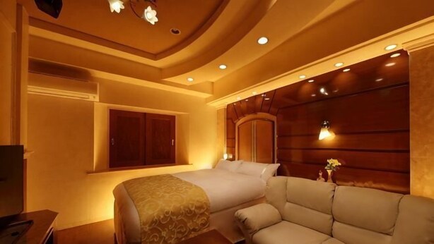 A hotel room with a bed, a sofa, a wooden headboard, and a window. - Hotel Fine Garden Kosei (Adult Only) (Konan)