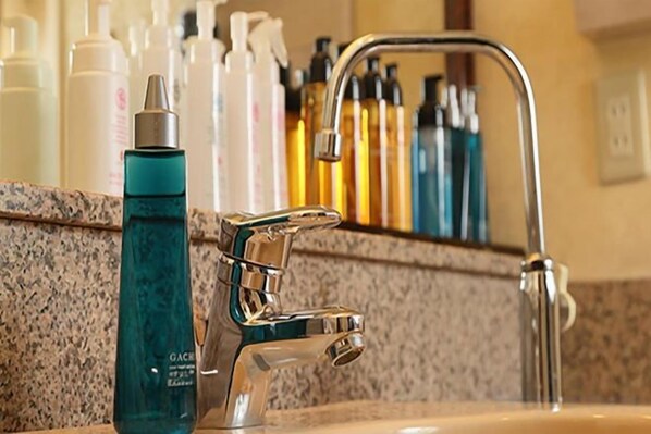 A bathroom sink with a chrome faucet, a bottle of blue liquid soap, and various toiletries in the background.