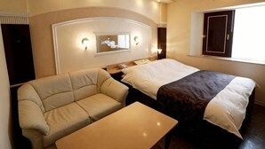 A hotel room with a bed, a sofa, a table, a headboard with lights, a window, and a wall-mounted TV. - Hotel Fine Garden Kosei (Adult Only) (Konan)
