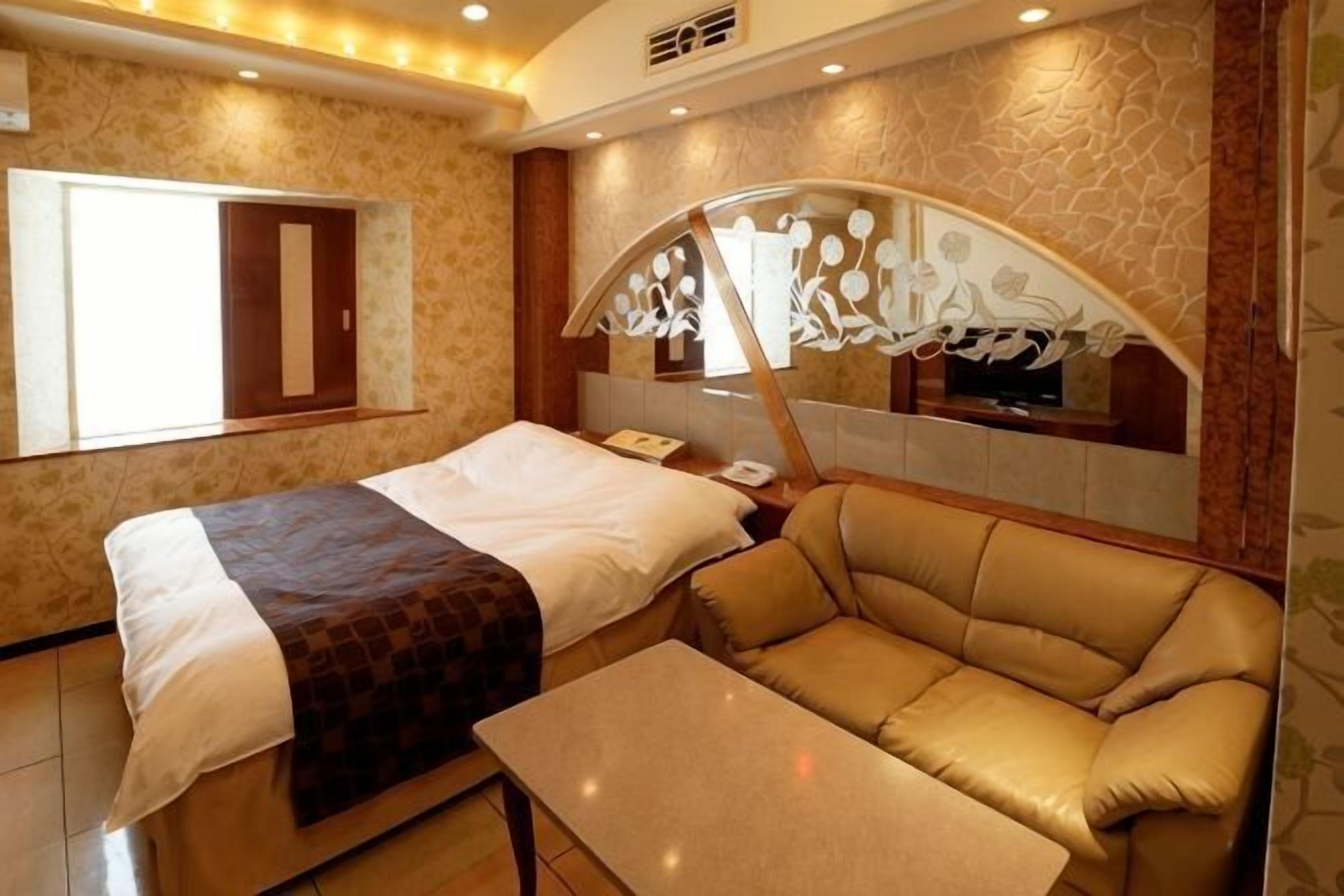 A hotel room with a bed, a sofa, a table, a mirror, and a window.
