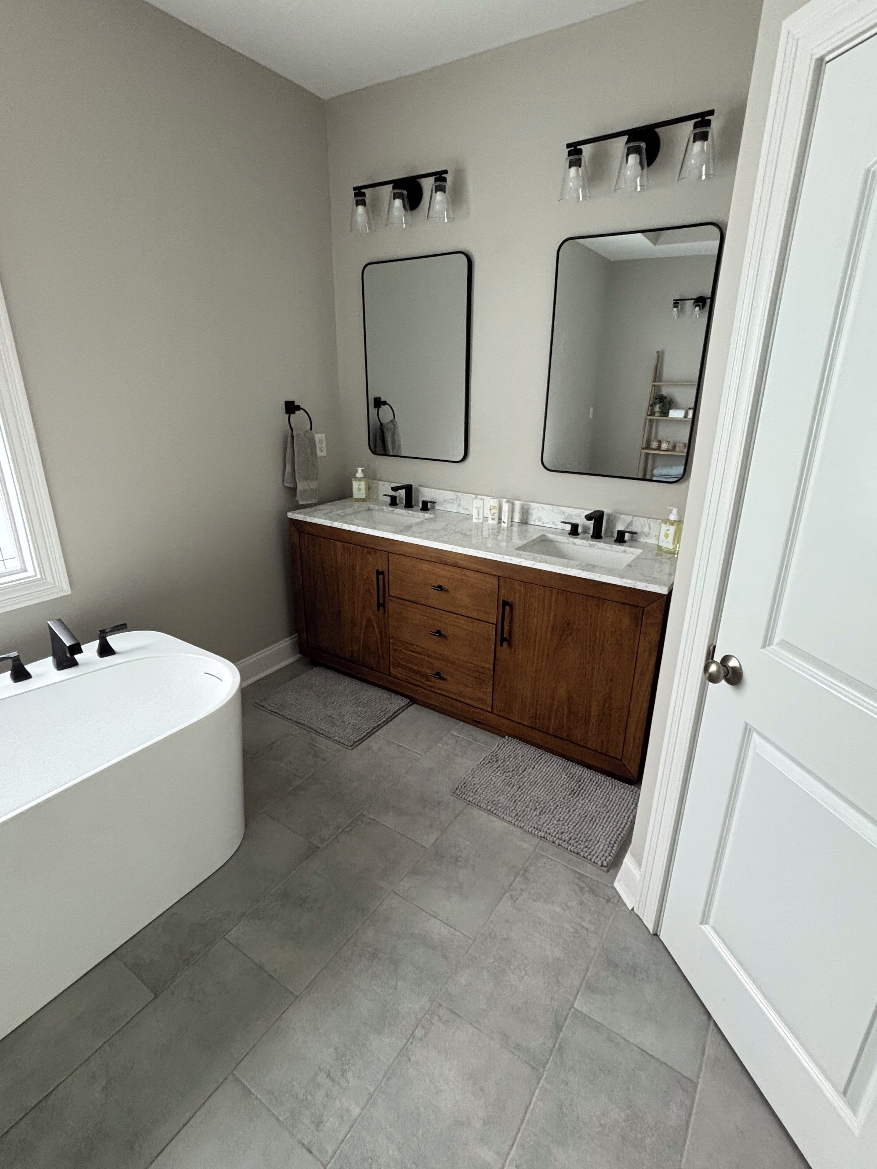 A modern bathroom with a freestanding bathtub, two sinks, and a large mirror.