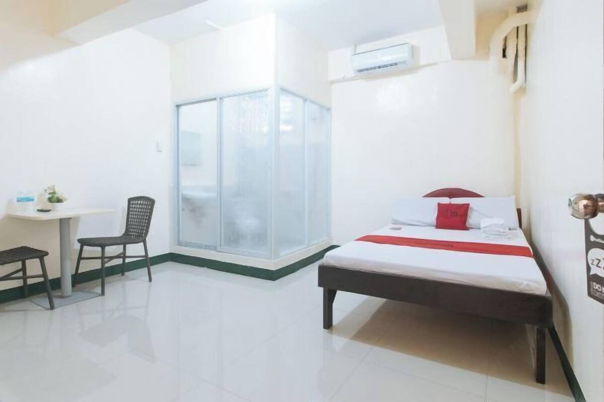 Habitación de hotel con cama, escritorio, silla y puerta corrediza de vidrio que da a un balcón.