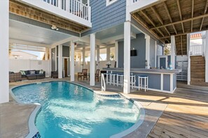 Zona de piscina con jacuzzi, bar y mobiliario exterior.