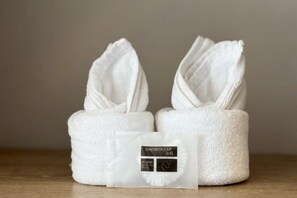 Dos toallas blancas con una etiqueta que dice 'SHOWER CAP' y un pequeño paquete blanco.