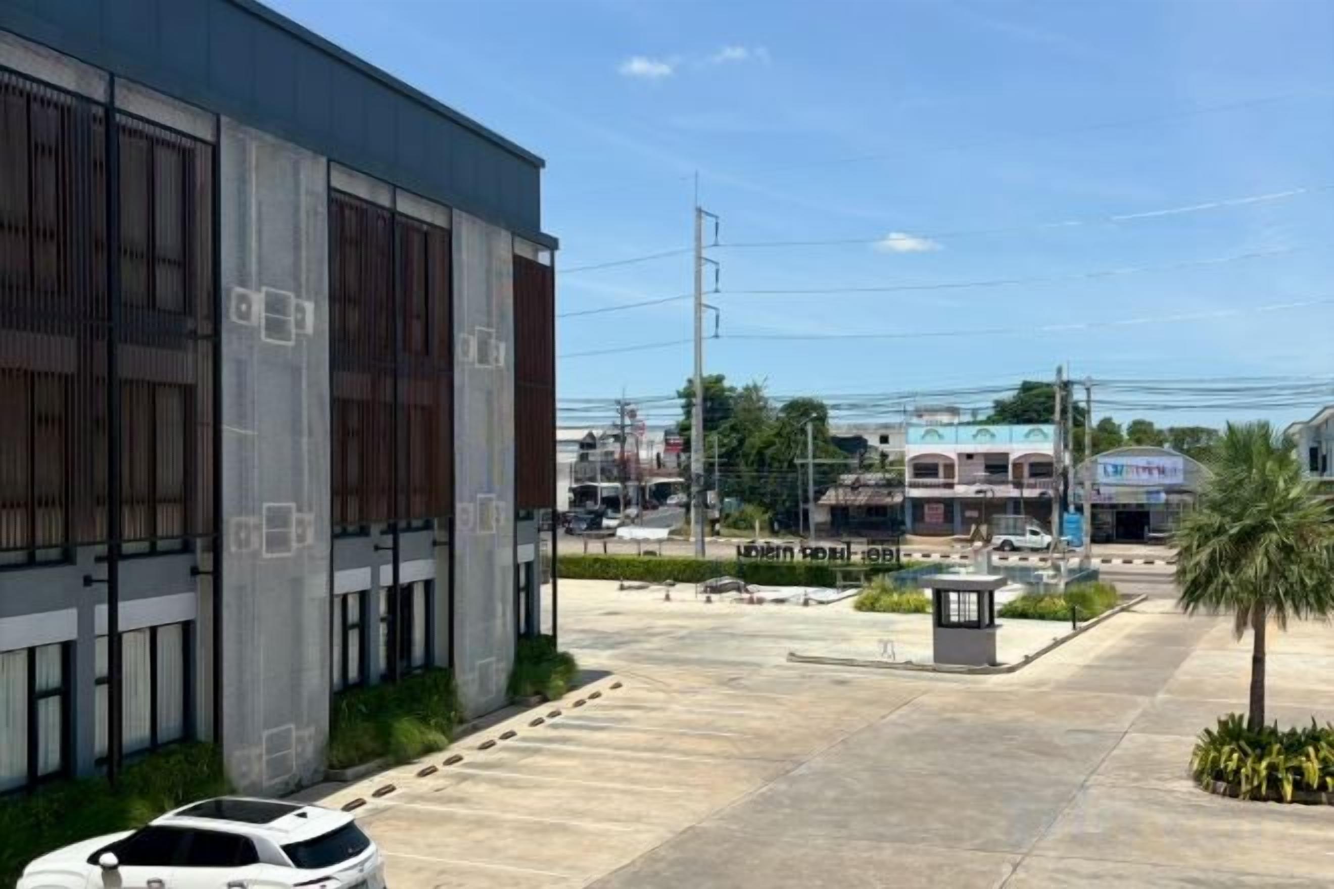 Un estacionamiento con un edificio a la izquierda, un pequeño quiosco en el centro y una palmera a la derecha.