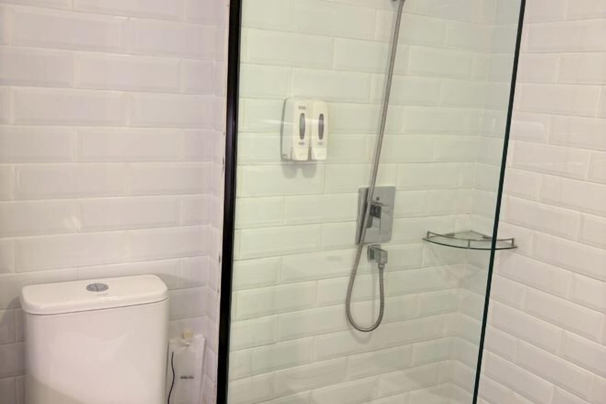 A glass-enclosed shower with a handheld showerhead, a glass shelf, and a white toilet.