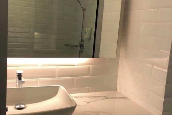 Une salle de bain avec un lavabo blanc, un miroir et une cabine de douche en verre.