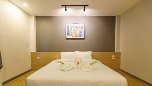 A hotel room with a neatly made bed, a framed artwork on the wall, and a wooden headboard. - The Model Garden (Yasothon)