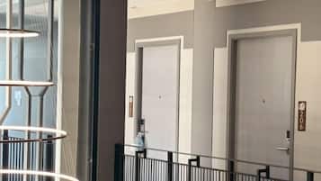 Pasillo de hotel con tres puertas, una escalera y una barandilla.