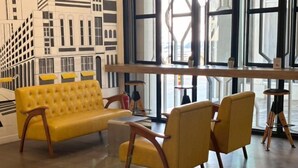A yellow sofa and chairs in a room with large windows and a cityscape mural. - The Model Garden (Yasothon)