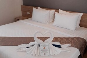 A hotel room with a neatly made bed, a wooden headboard, and a heart-shaped towel arrangement on the bed. - The Model Garden (Yasothon)