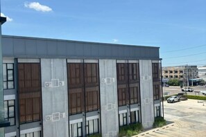 A modern building with large windows and a parking lot in the foreground. - The Model Garden (Yasothon)