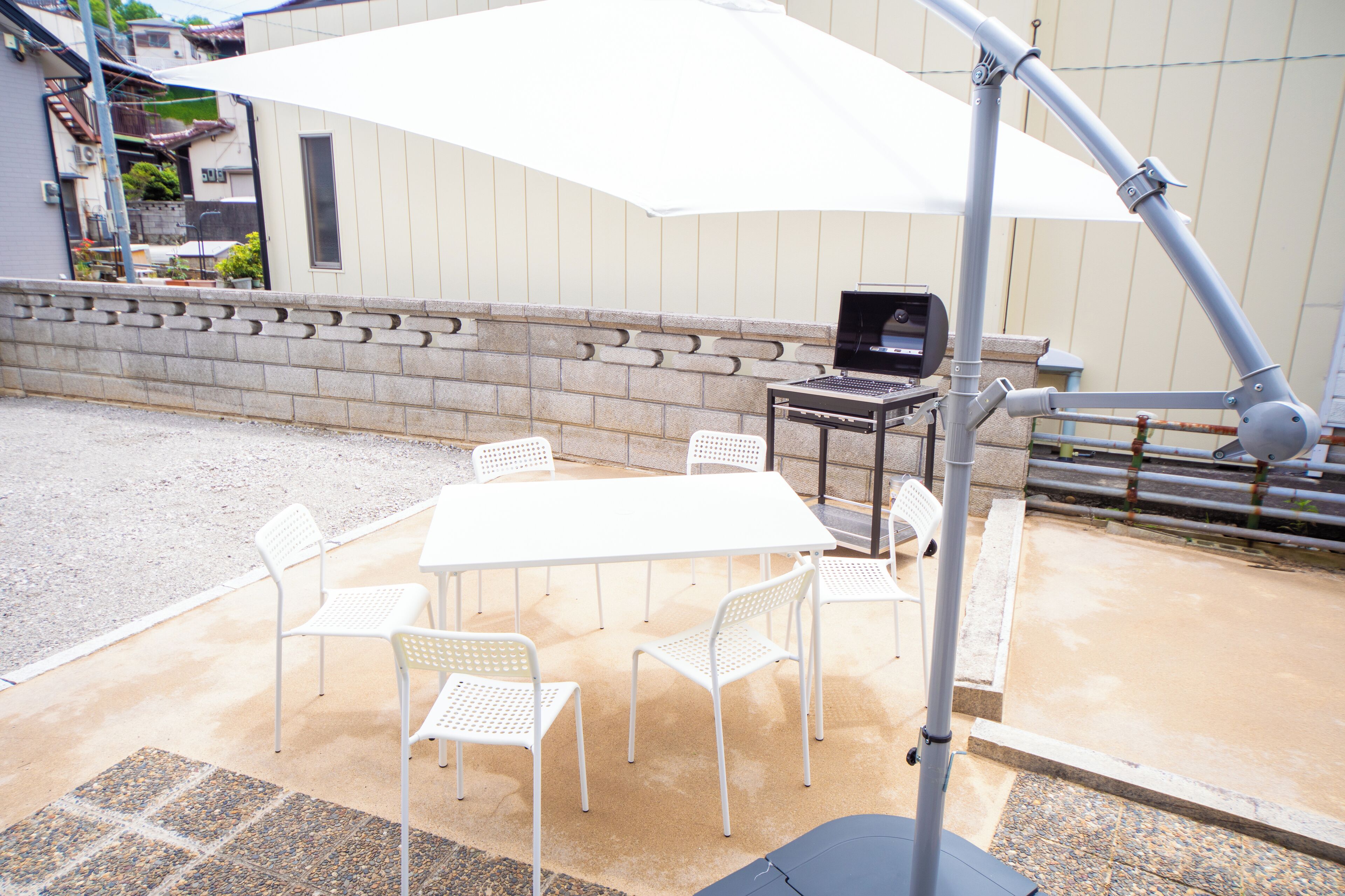 An outdoor patio with a white table and chairs, a barbecue grill, and a large umbrella.