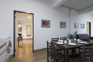 A dining area with a wooden table set for four, surrounded by chairs. There are framed artworks on the walls. - Polaris Suite (Kota Kinabalu)
