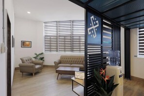 A modern living room with a sofa, armchair, coffee table, and a water dispenser. - Polaris Suite (Kota Kinabalu)