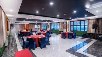 A conference room with multiple tables and chairs, large windows, and a stage with a screen.