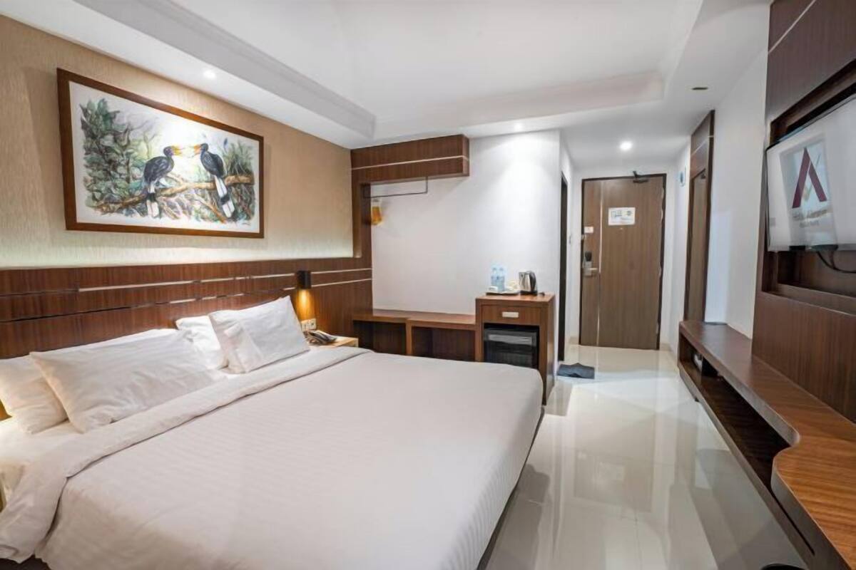 A hotel room with a bed, a desk, a TV, and a painting on the wall.