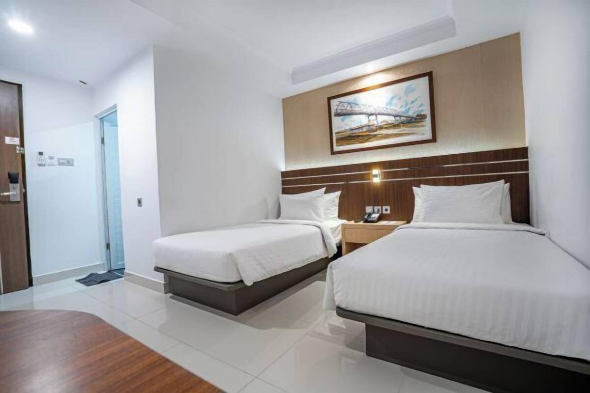 A hotel room with two beds, a wooden floor, a painting on the wall, and a nightstand with a phone.