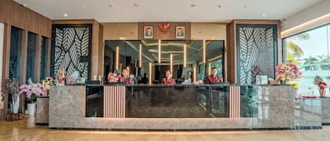 A hotel reception area with a marble counter, staff behind it, and large windows.