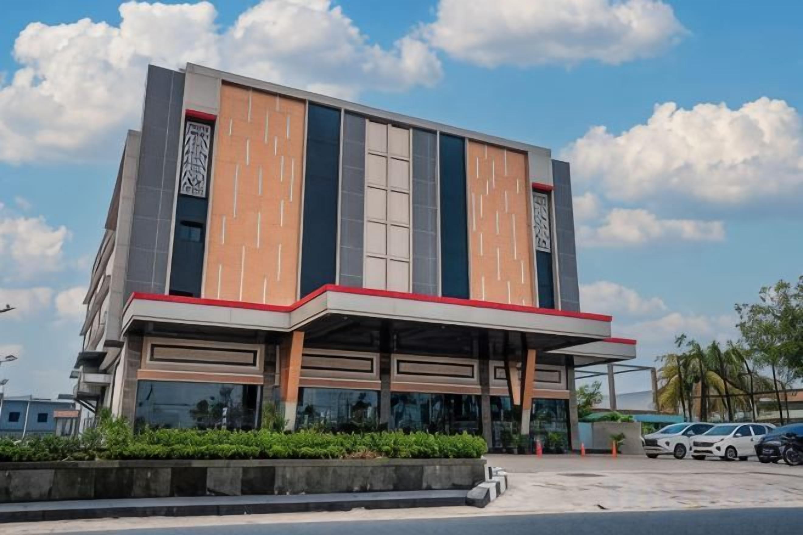 A modern building with a flat roof, large windows, and a parking area in front.