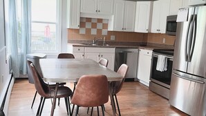 A modern kitchen with white cabinets, a stainless steel refrigerator, and a wooden dining table with chairs. - Cozy 3 bedroom home with perfect location in Saint John (Saint John)