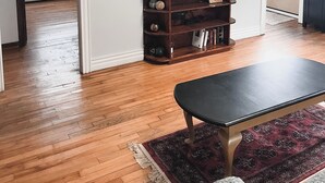 A living room with hardwood flooring, a dark wooden coffee table, a flat-screen TV mounted on the wall, and a dark wooden entertainment center. - Cozy 3 bedroom home with perfect location in Saint John (Saint John)