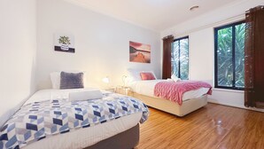 A bedroom with two beds, a large window, and artwork on the walls.