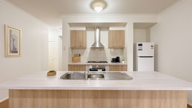 A modern kitchen with a central island, stainless steel sink, wooden cabinets, and a built-in oven.