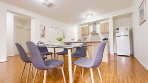 A modern kitchen with wooden cabinets, a white refrigerator, and a dining area with a glass table and purple chairs.