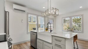 A modern kitchen with a central island, stainless steel appliances, and large windows with blinds.