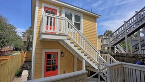A two-story house with a red door, white railings, and a wooden deck.