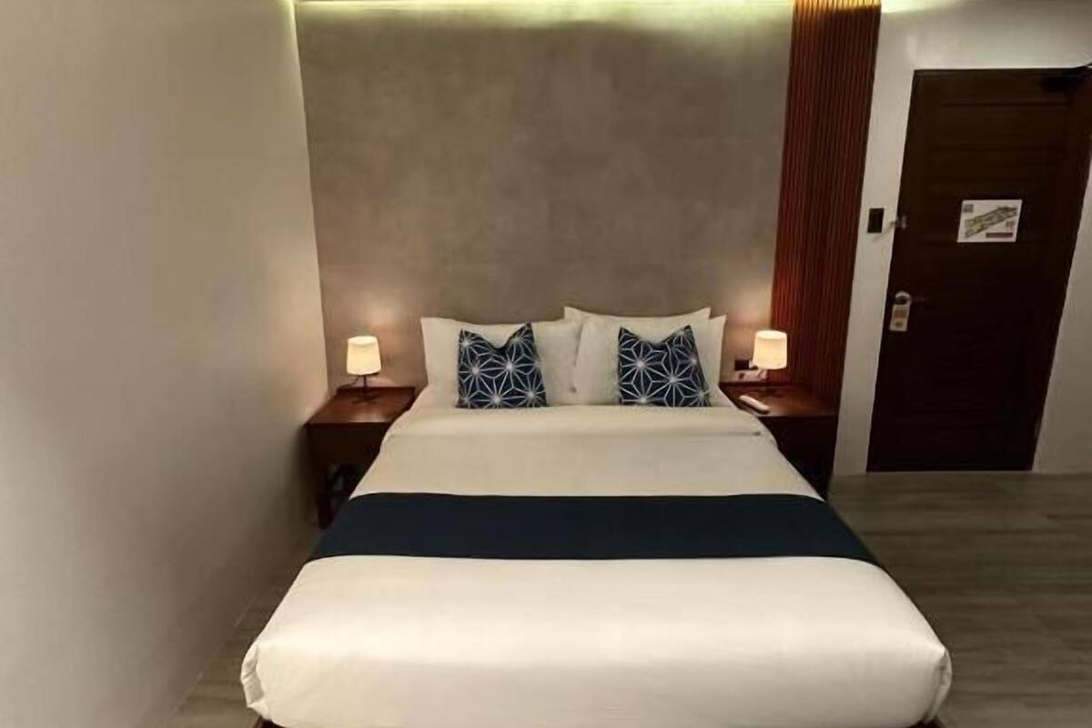 A modern hotel room with a large bed, bedside lamps, and a door.