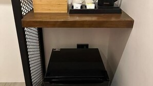 A compact kitchenette with a coffee maker, a bottle, and a tray of mugs on a wooden shelf. - Coron 180 Hotel (Coron)