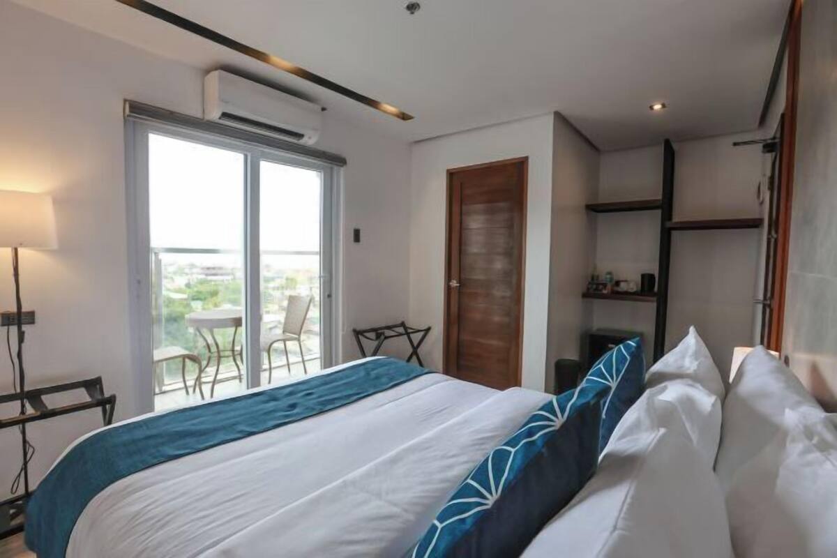 A modern hotel room with a bed, a desk, a chair, and a balcony with a view.