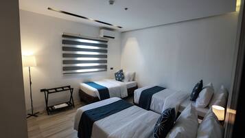 A modern hotel room with two beds, a standing lamp, a radiator, and a window with blinds.