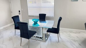 A dining area with a glass table, four chairs, a blue bowl, a white door, and a window with blinds. - Charming  Two bedroom house near Beaches and Tampa Bay attractions. (Oldsmar)