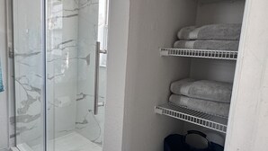 A bathroom with a glass-enclosed shower, marble walls, and a towel rack with neatly folded towels. - Charming  Two bedroom house near Beaches and Tampa Bay attractions. (Oldsmar)