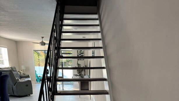 A staircase with dark wooden steps and black railings, leading to a room with a white ceiling and a ceiling fan. - Charming  Two bedroom house near Beaches and Tampa Bay attractions. (Oldsmar)