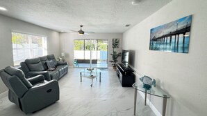 A spacious living room with a sofa, coffee table, and a painting of a bridge. - Charming  Two bedroom house near Beaches and Tampa Bay attractions. (Oldsmar)