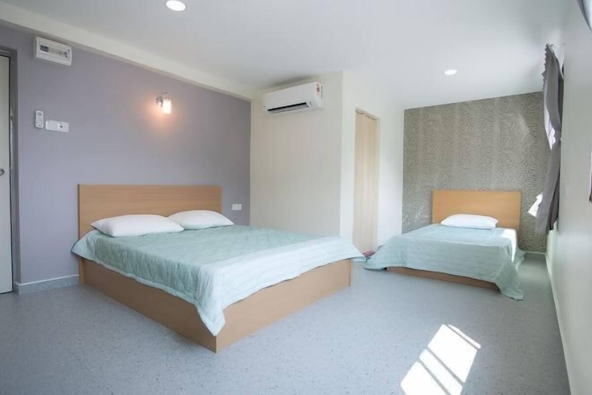 A hotel room with two beds, an air conditioning unit, and a wall-mounted light fixture.