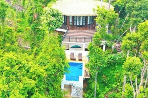 A resort with a thatched-roof building, a swimming pool, and lush greenery surrounding the property.