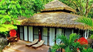A thatched-roof structure with a wooden deck, two lounge chairs, and a table with chairs. - Lihim Resorts (El Nido)