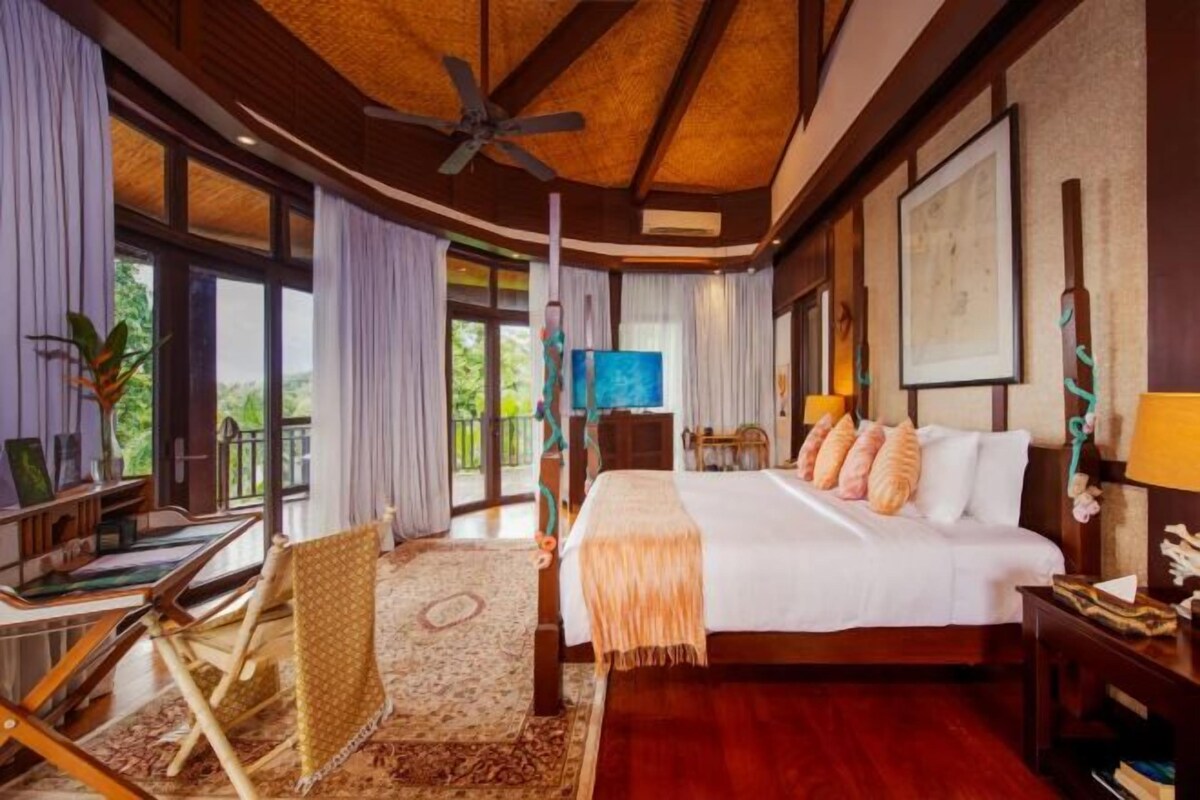A hotel room with a bed, a desk, a chair, a TV, and large windows.