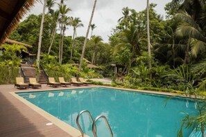 A swimming pool with lounge chairs and a wooden deck, surrounded by palm trees and greenery. - Lihim Resorts (El Nido)