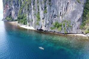 A coastal cliff with a boat on the water. - Lihim Resorts (El Nido)