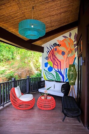 A covered outdoor seating area with wicker chairs, a white sofa, and a colorful mural on the wall. - Lihim Resorts (El Nido)