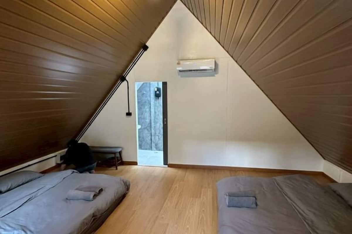 Una habitación pequeña con techo inclinado, dos camas, un banco y una puerta que da al exterior.