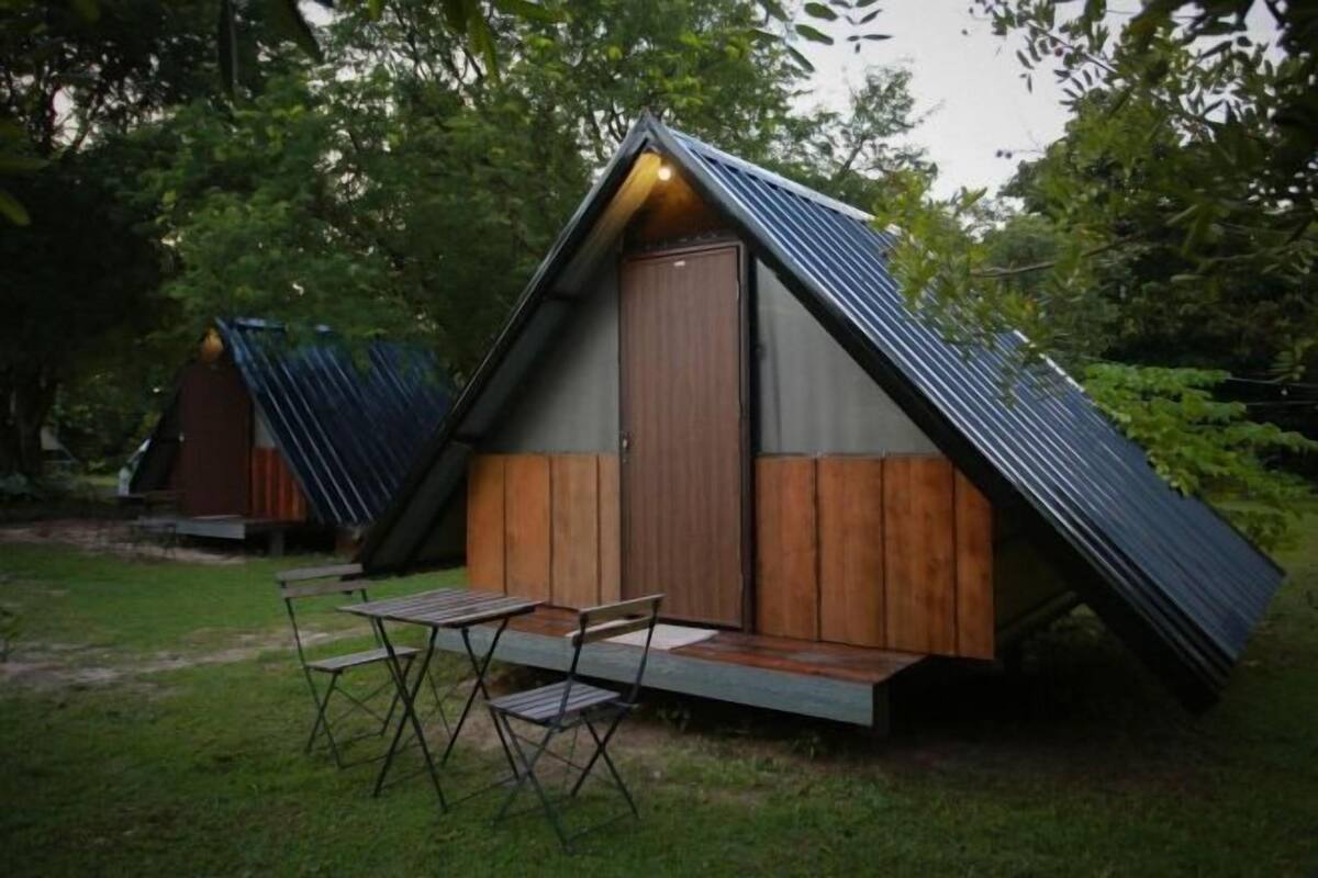 Una pequeña estructura de madera triangular con techo inclinado, una puerta y una mesa con sillas afuera.